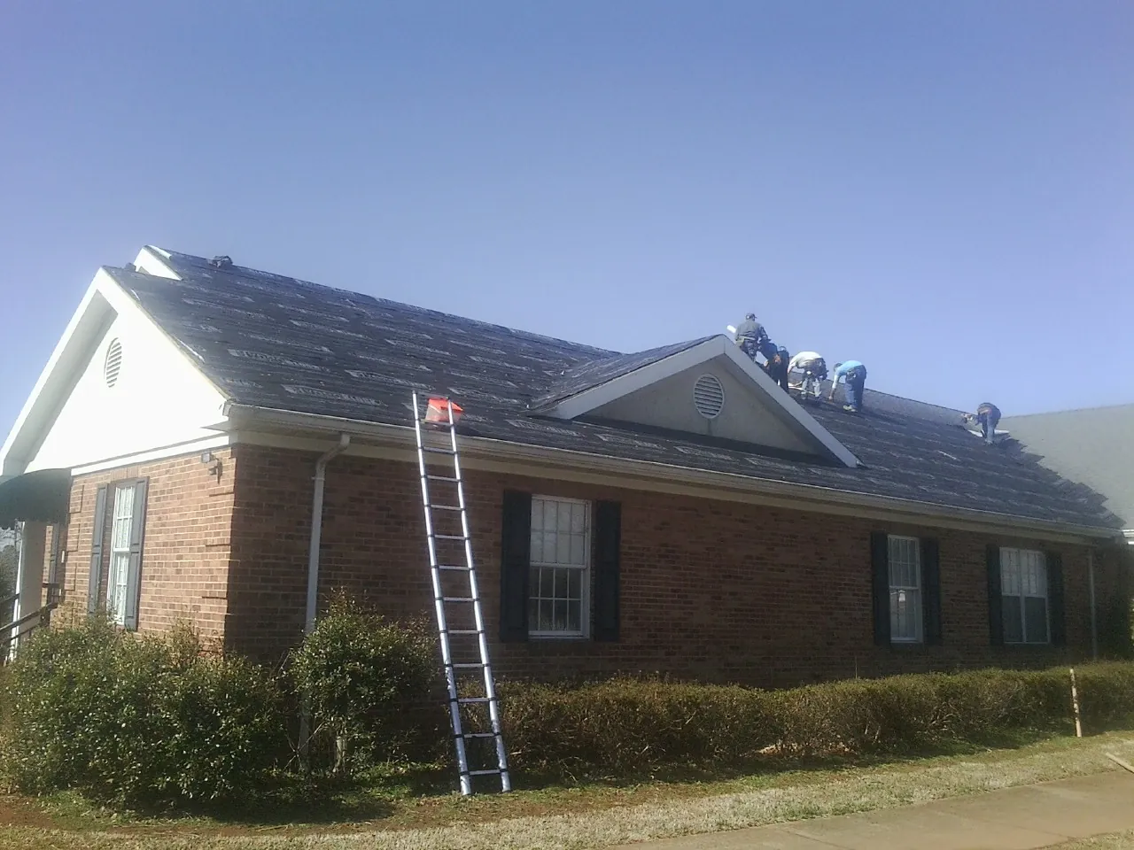 Crew tearing shingles off a brick ranch roof with a ladder set — Emergency Roof Repair work by our crew in Old Greenwich