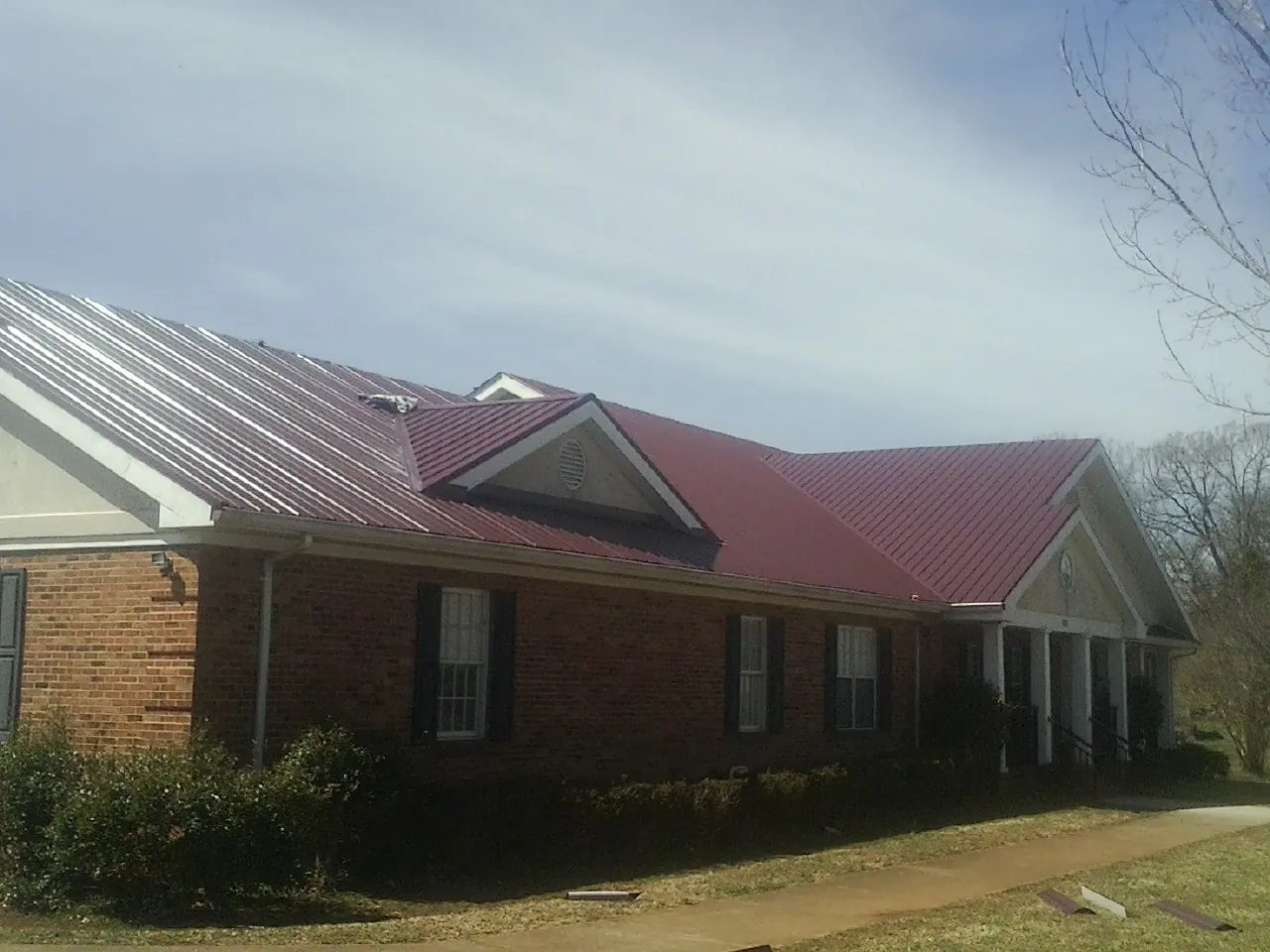 Red metal roof with gabled entries on a long brick building, from a Hail Damage Roof Repair job in Old Greenwich