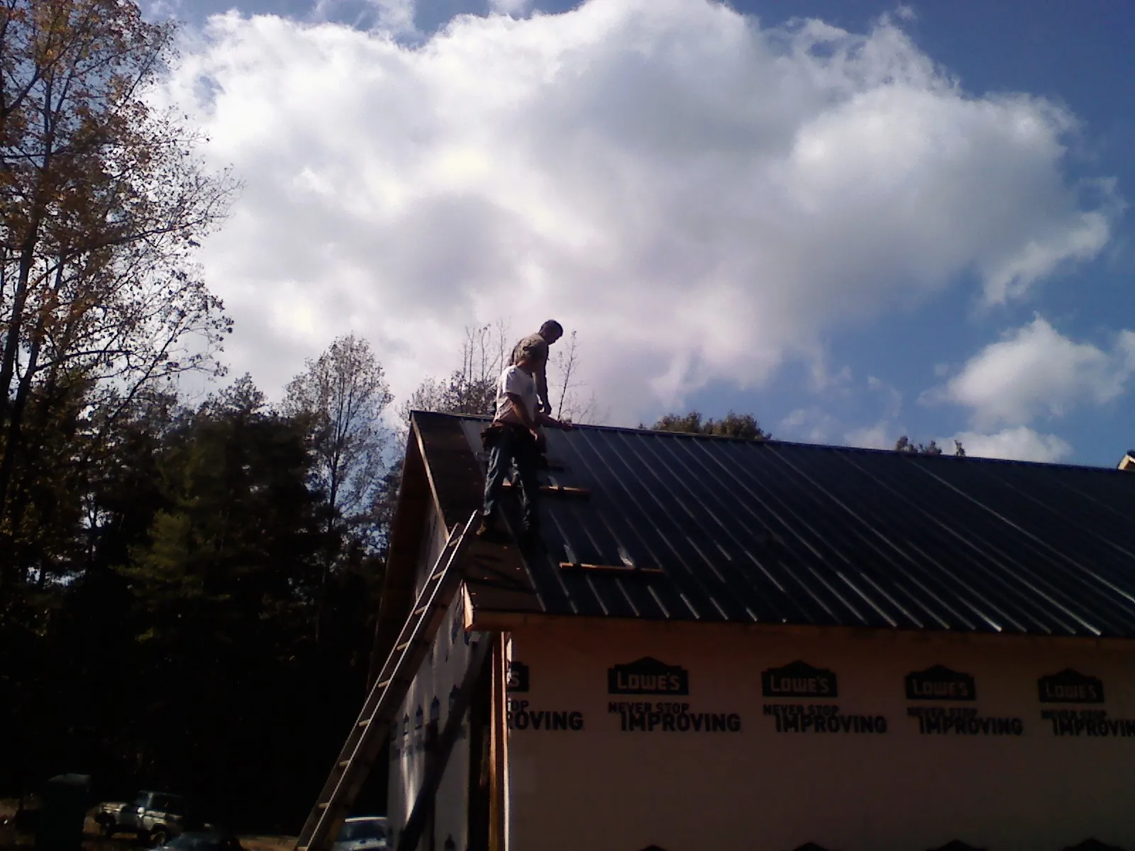 Roofer fastening dark metal panels high against a cloudy sky, from a Roof Inspection job in Old Greenwich