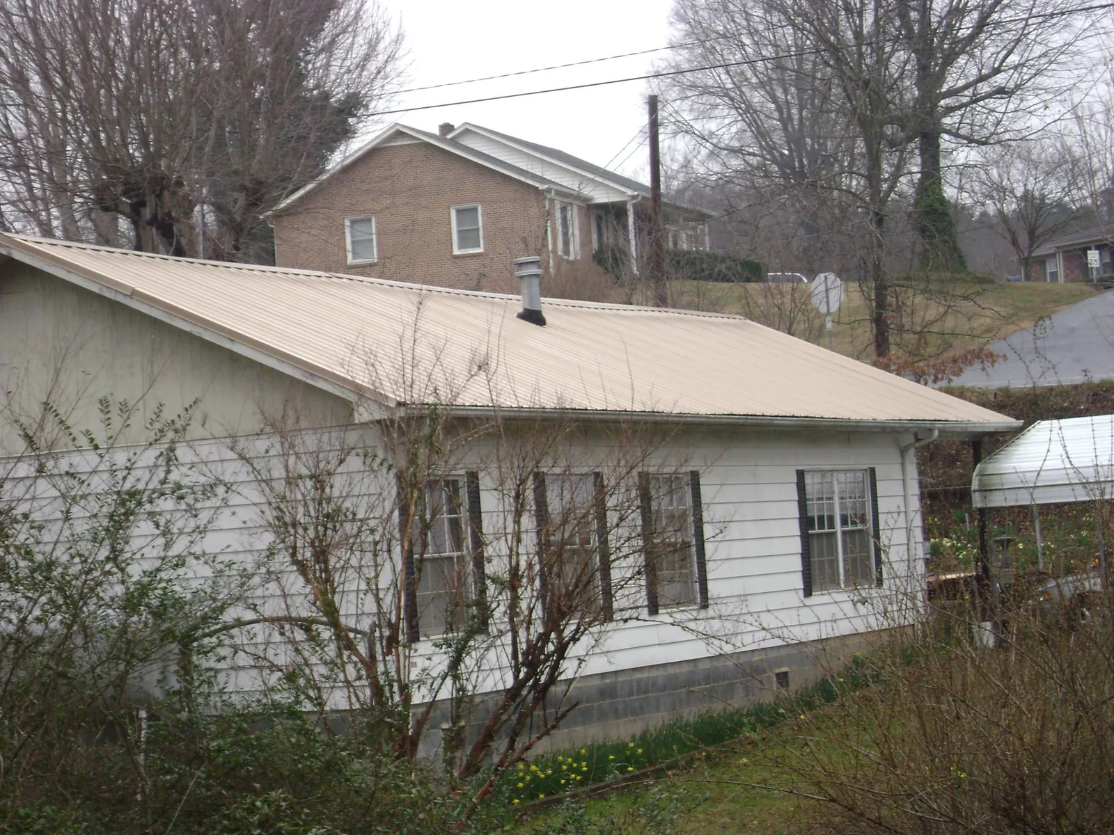 Tan metal roof on a white sided house set into a hillside — Commercial Roofing by Roofing Brothers in Old Greenwich